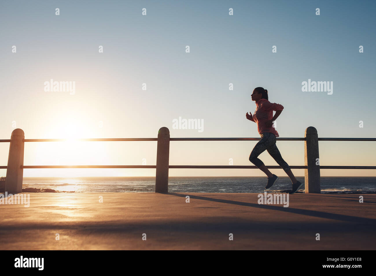 Immagine di montare sportive jogging su una strada dal mare durante la sera. Femmina formazione runner al tramonto. Foto Stock