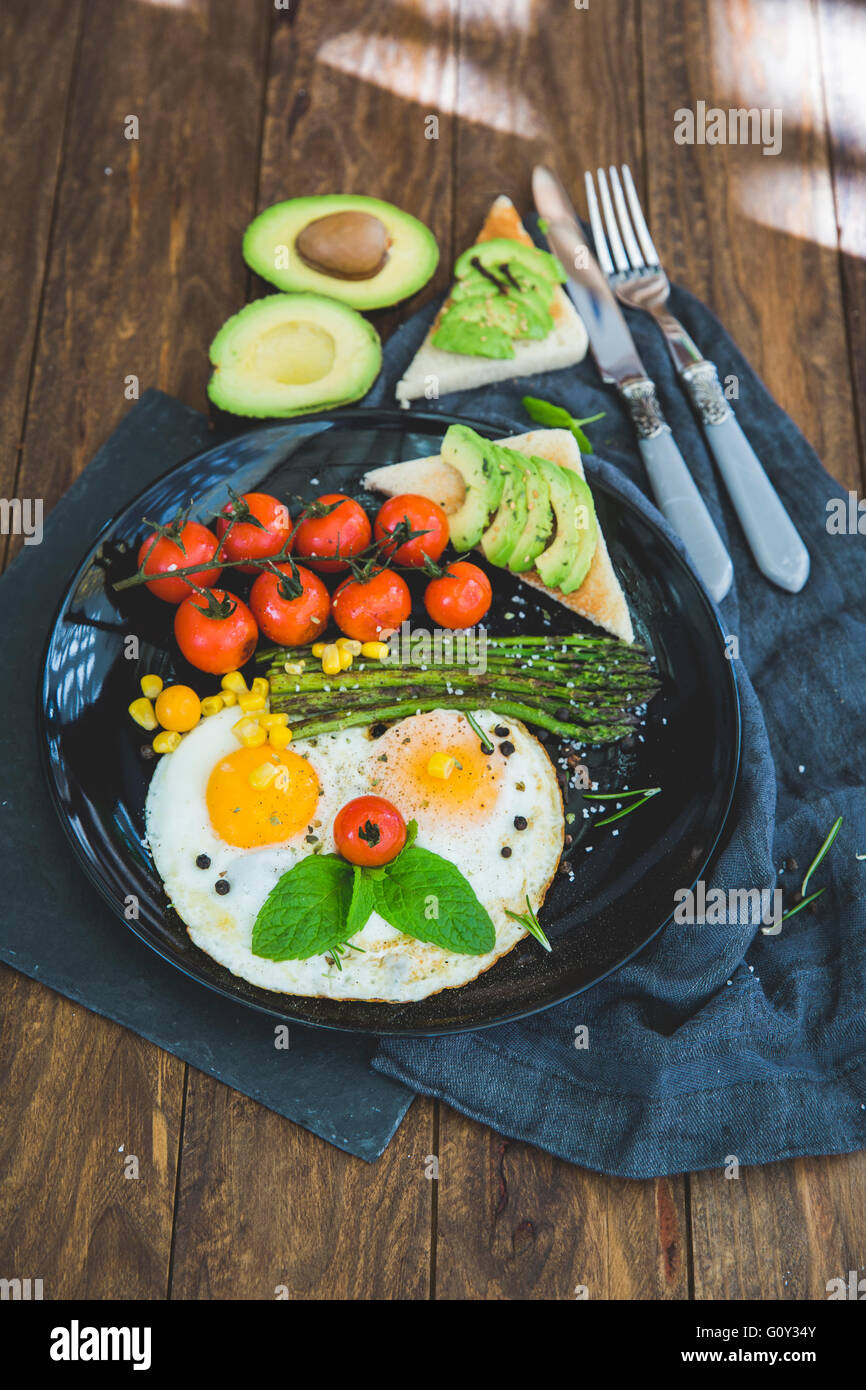 Uova fritte, pomodori ciliegini, avocado, asparagi e toast prima colazione Foto Stock