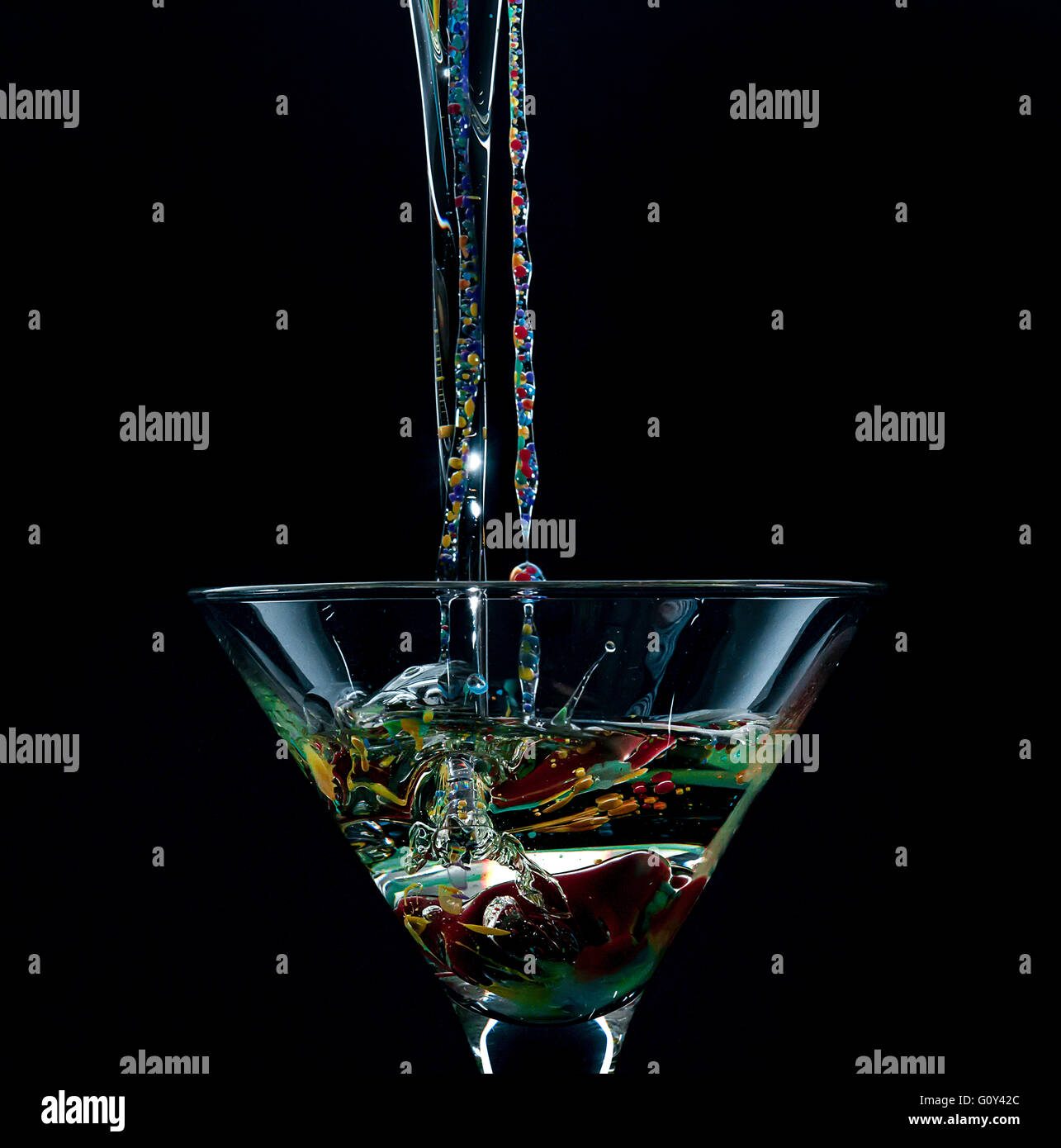 Acqua, olio e vernici acriliche versando in Martini cocktail glass Foto Stock