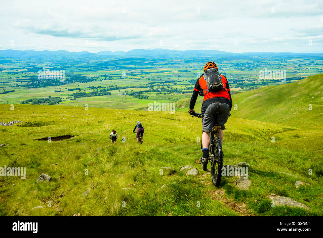 I ciclisti di montagna scendendo dalla croce cadde ridge in Pennines con il Lake District fells all'orizzonte Foto Stock