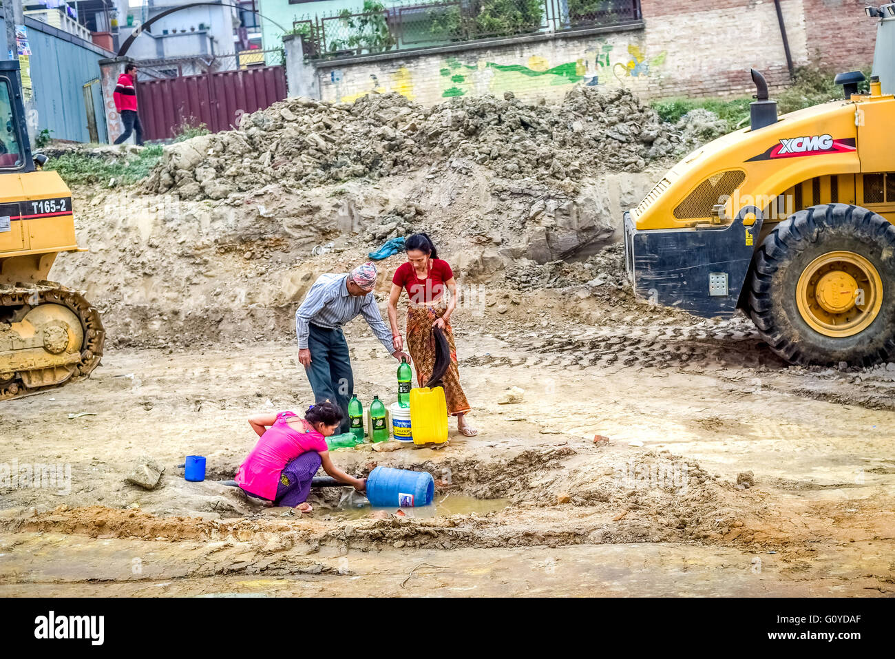 Una famiglia locale prende l'acqua da una linea d'acqua rotta durante la stagione secca a Kathmandu, un anno dopo i terremoti del Nepal del 2015. Foto Stock