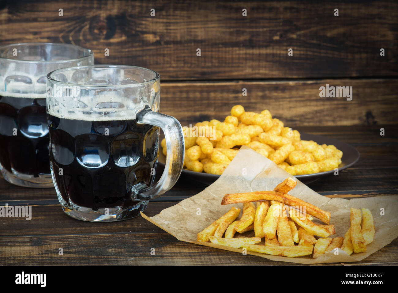 Due boccali di birra scura con patate fritte e sbuffi di arachidi su sfondo di legno Foto Stock