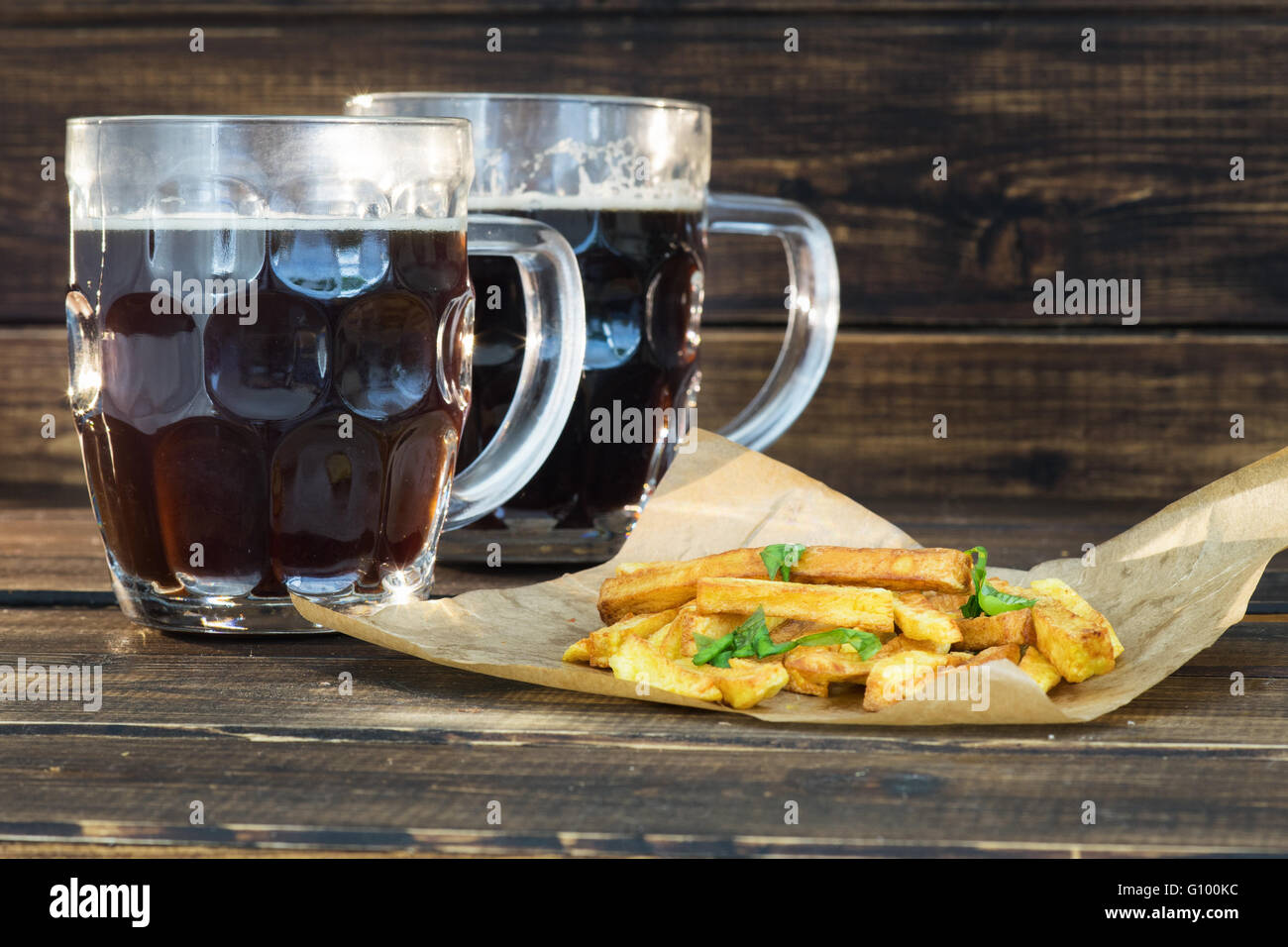 Due boccali di birra scura con patate fritte su sfondo di legno Foto Stock