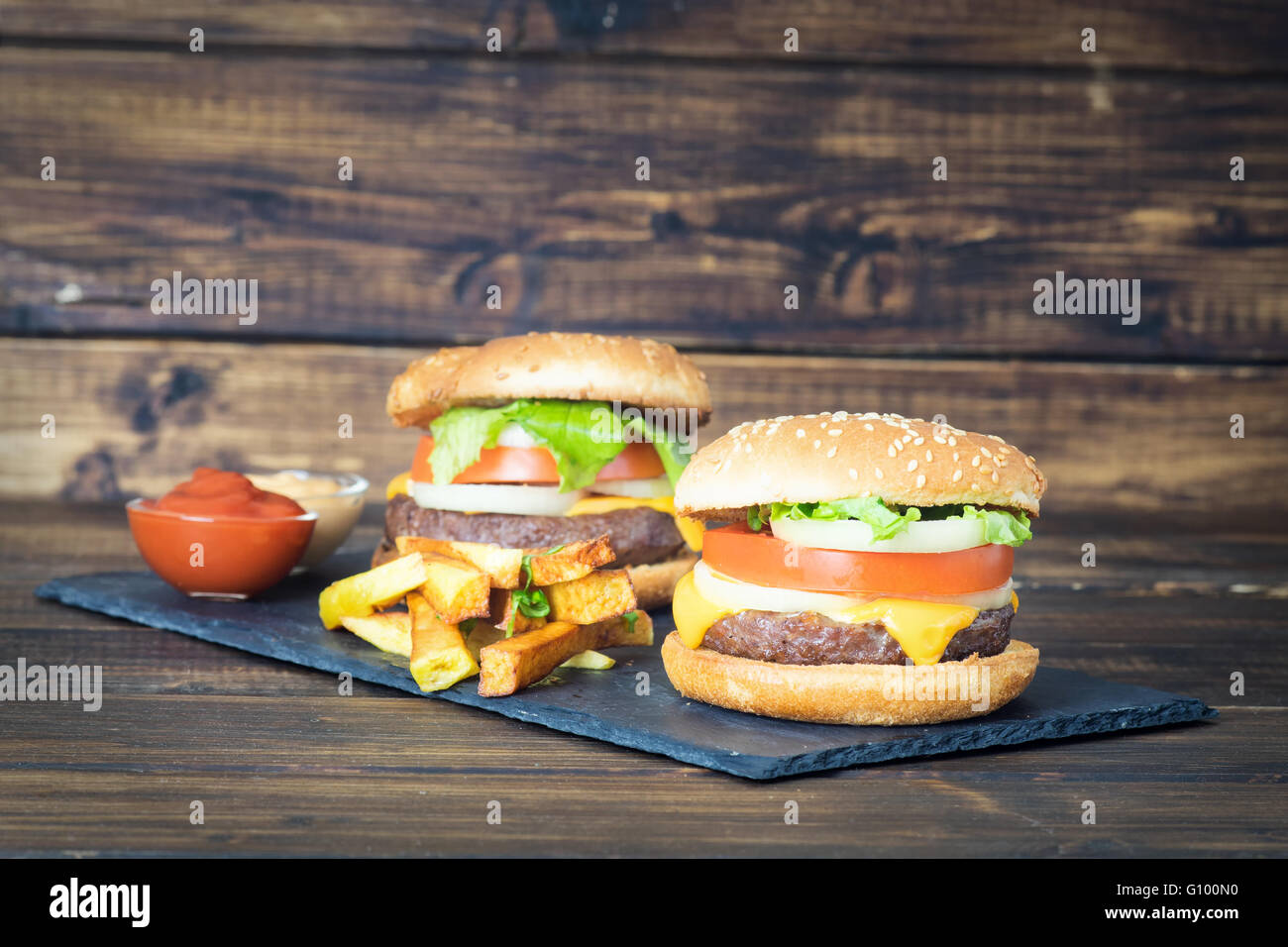 Due cheeseburger con patate fritte sulla piastra di ardesia e scuro dello sfondo in legno Foto Stock