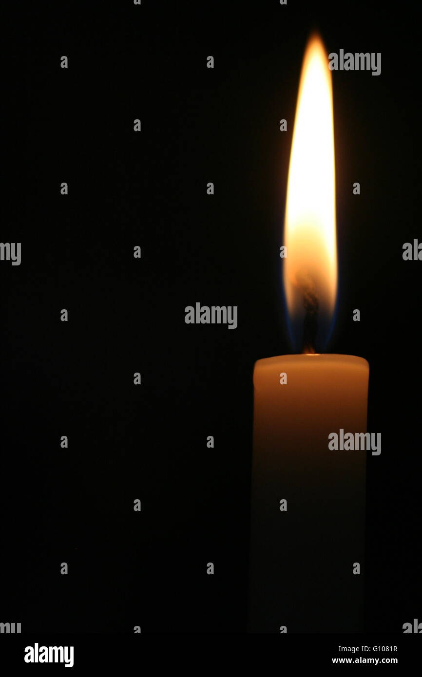 Candela contro uno sfondo nero in una chiesa Foto Stock