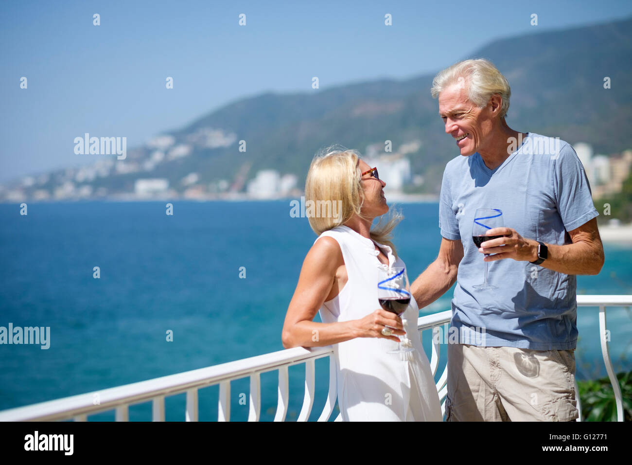 Senior l uomo e la donna godendo il vino rosso sul balcone della loro fronte oceano a casa in Messico. Foto Stock