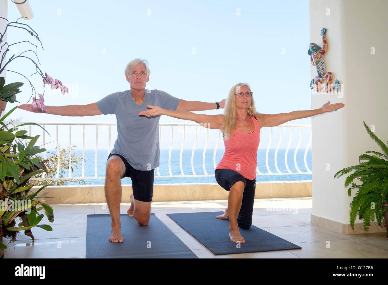 Senior l uomo e la donna che esercitano lo yoga sul balcone del loro Ocean front home Foto Stock