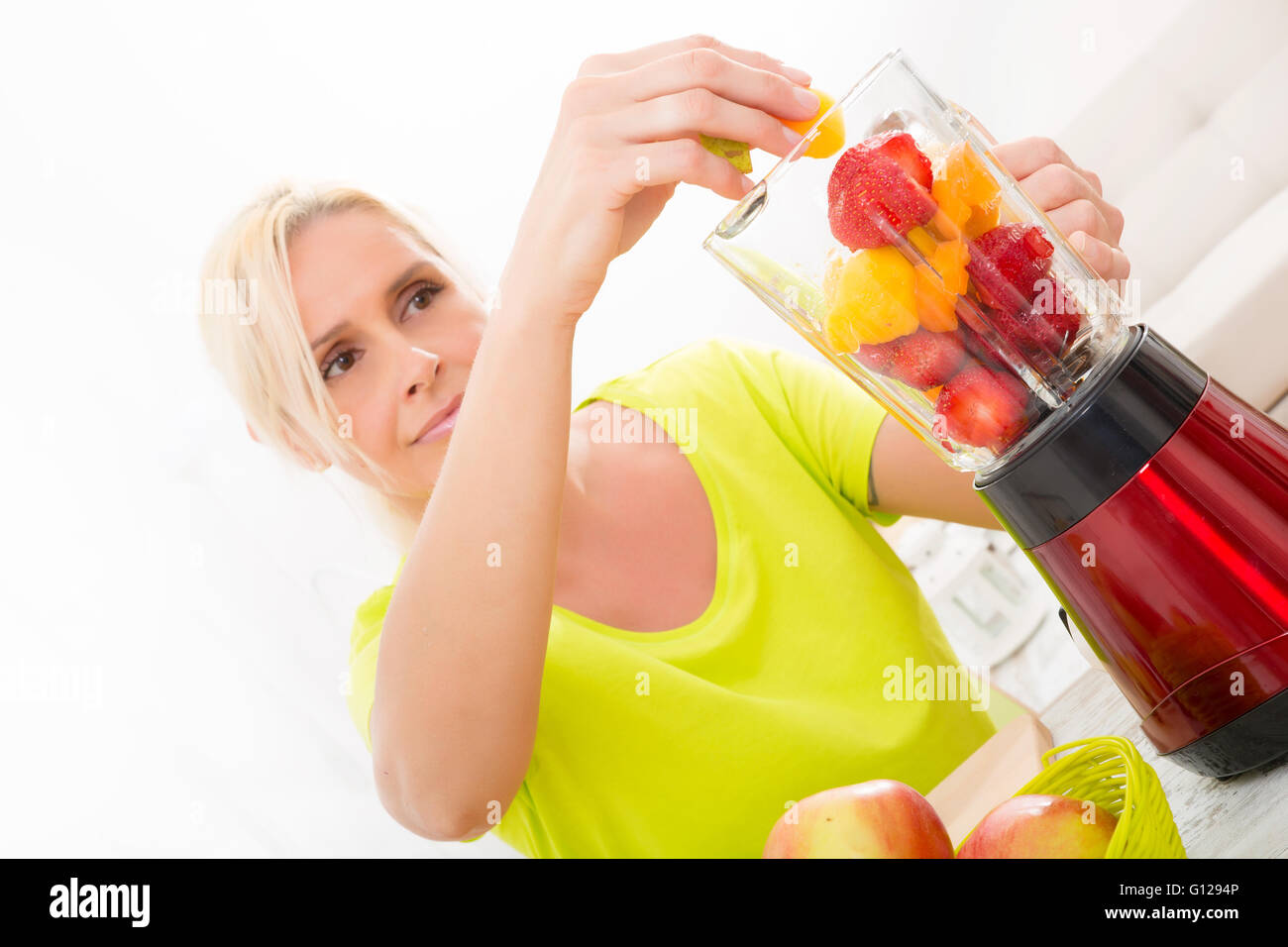 Una bella donna matura preparare un frullato o succo di frutta in cucina. Foto Stock