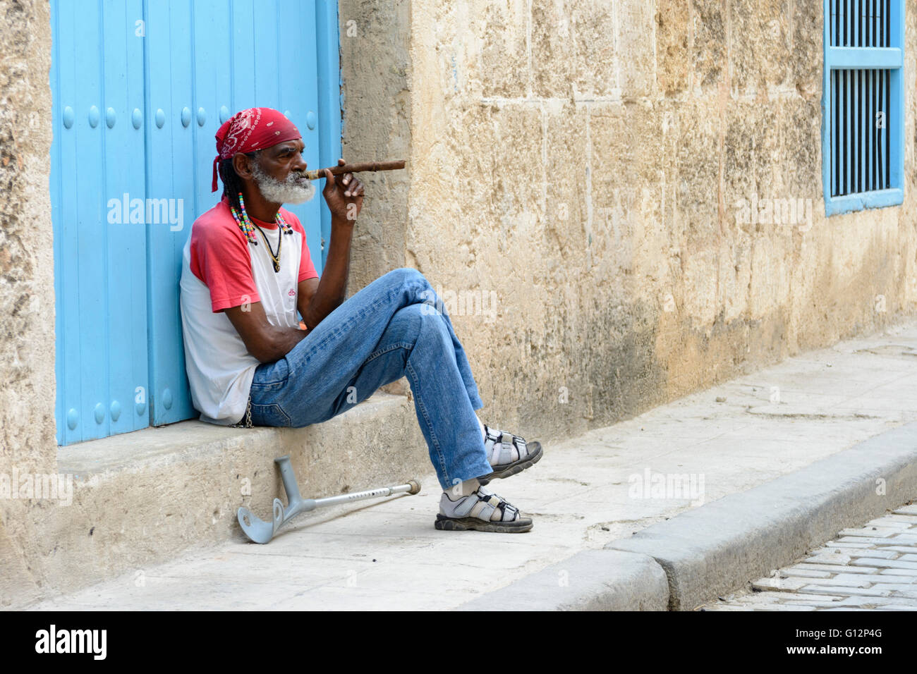 Un uomo anziano si siede su una fase di fumare un sigaro di grandi dimensioni a l'Avana Vecchia, Havana, Cuba Foto Stock