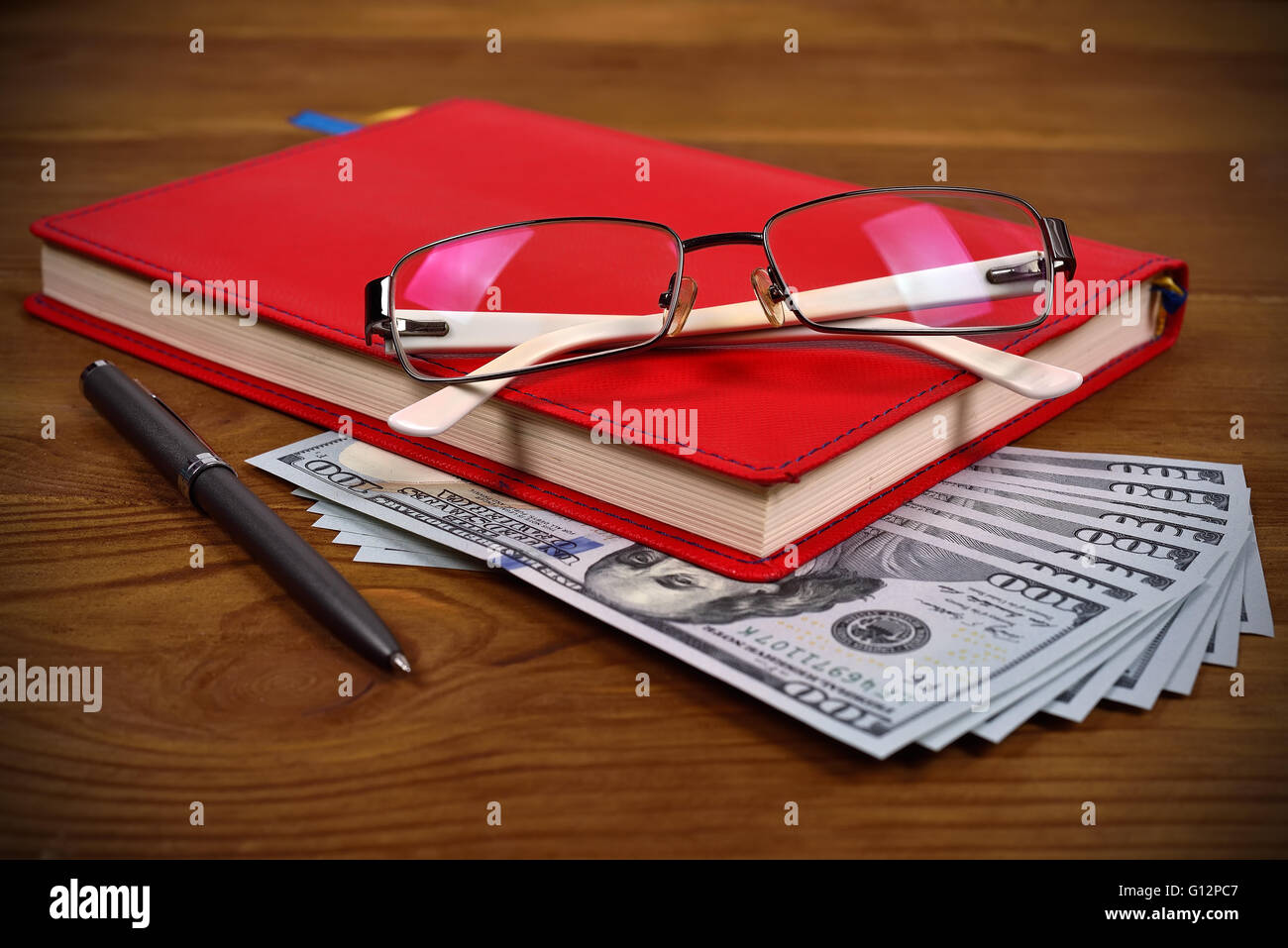 Rosso diario di cuoio, bicchieri, penna e le fatture del dollaro sulla scrivania in legno Foto Stock