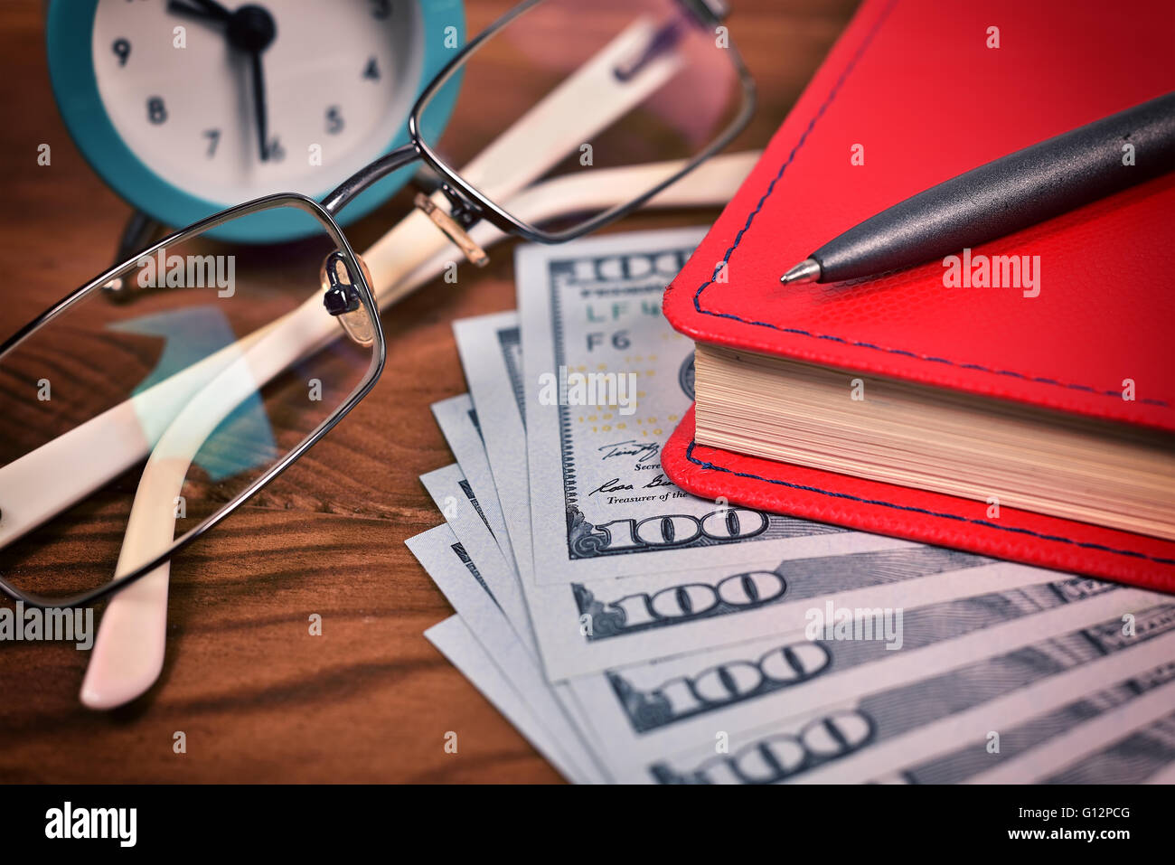 Diario rosso, bicchieri, penna, dollaro e orologio sulla scrivania in legno Foto Stock