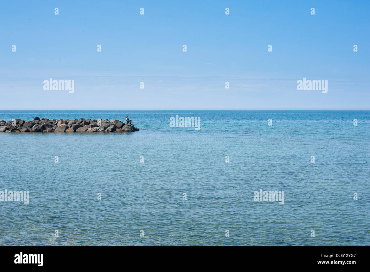Fisherman solo sulla roccia e grande blu del mare paesaggio nella soleggiata giornata estiva Foto Stock