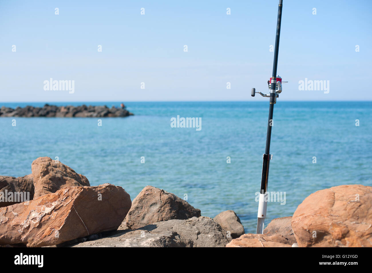 Canna da pesca con mulinello rosso dettaglio con il blu del mare e del cielo al di fuori della messa a fuoco lo sfondo Foto Stock