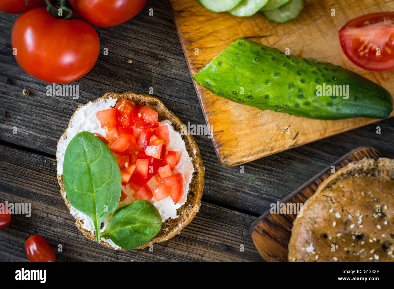 Snack sani: pane piatto, crema di formaggio, pomodori e baby spinaci. Tabella vista dall'alto il cibo, laici piatta Foto Stock