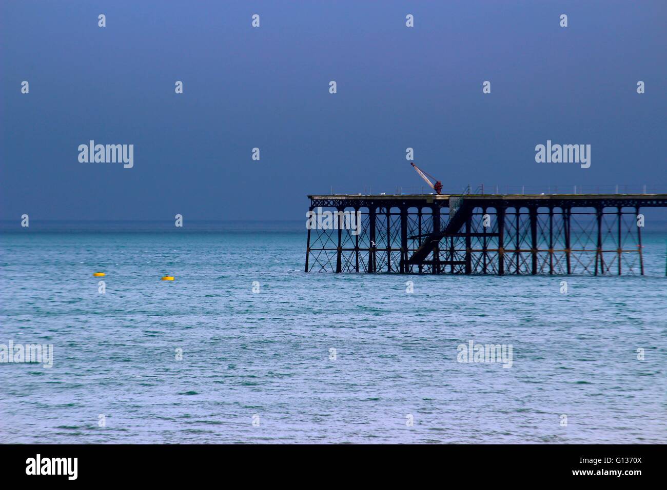 Vittoriano fatiscente molo di ferro con una gru fotografati contro un blu scuro cielo tempestoso e increspato azzurro del mare Foto Stock