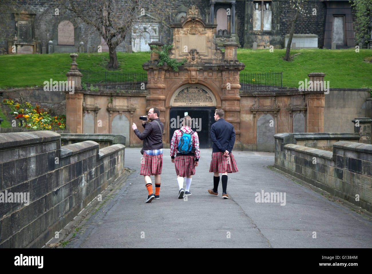 Tre turisti maschio a piedi attraverso il ponte dei sospiri sporting omaggio costumi nelle necropoli di Glasgow, Scotland, Regno Unito Foto Stock