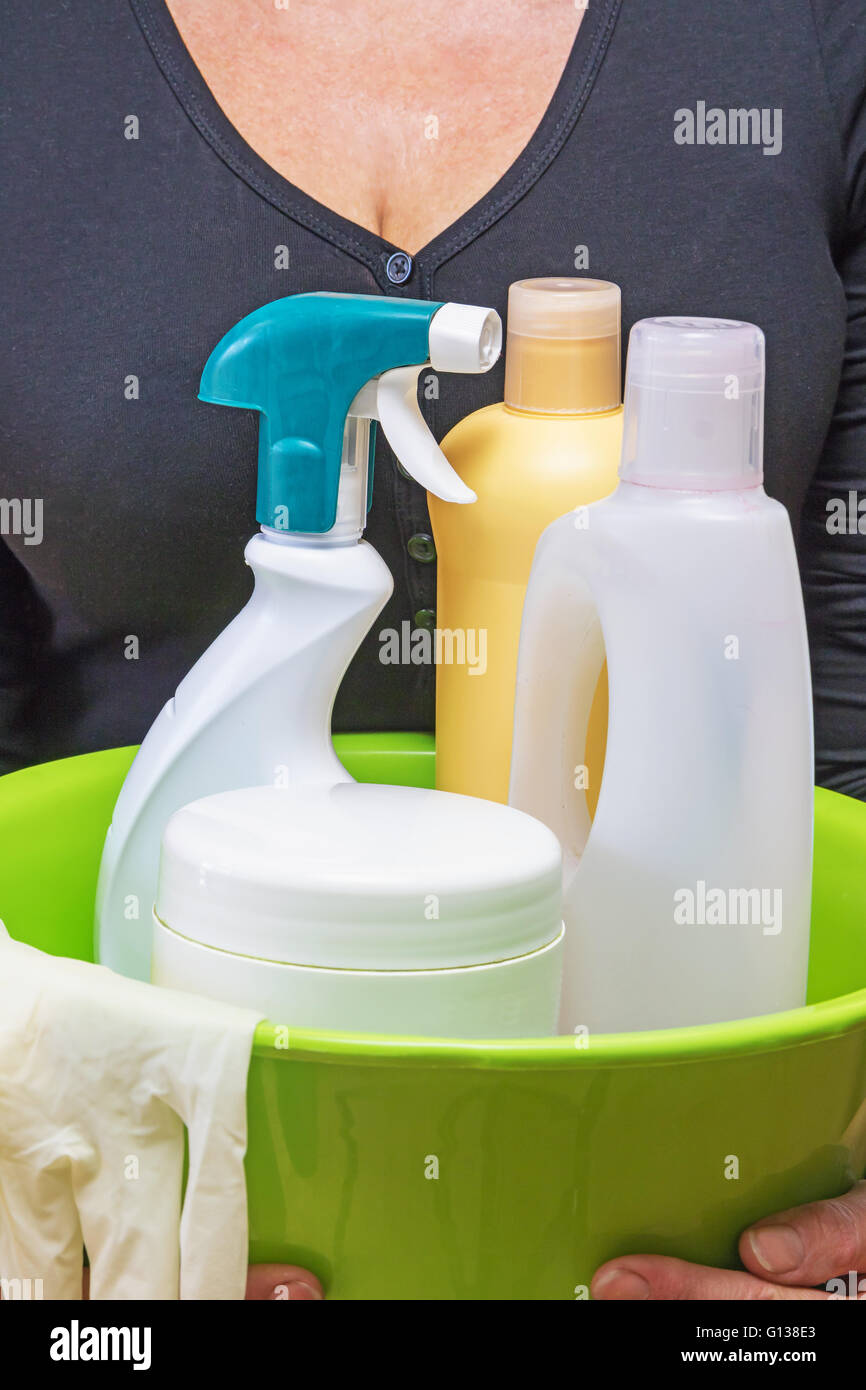 La donna è in possesso di detergenti per uso domestico. Le bottiglie di plastica, spray, guanti di gomma, tutti nel verde della vasca in plastica. Foto Stock
