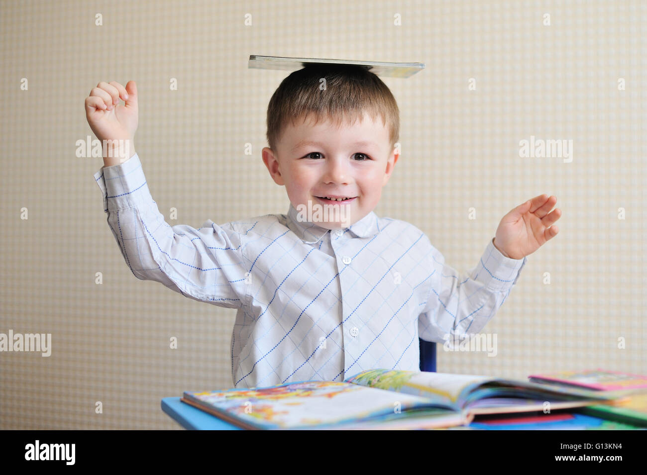 Giovani schoolboy giocando con libri e sorridente come egli siede alla sua scrivania in aula Foto Stock