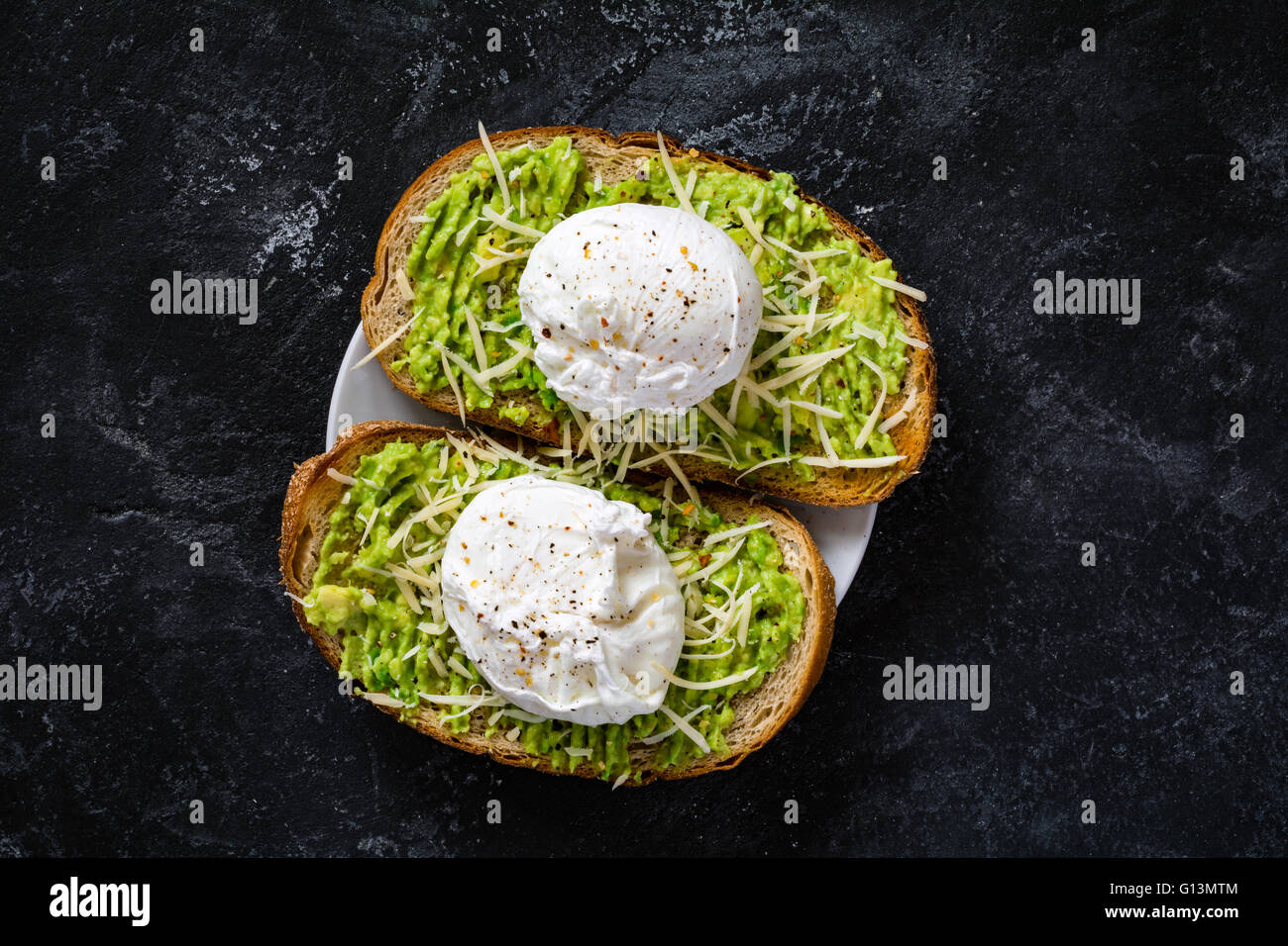 Due fette biscottate con la purea di avocado, formaggio e uova in camicia su scuro sfondo testurizzato, vista dall'alto. Sana colazione o uno spuntino Foto Stock