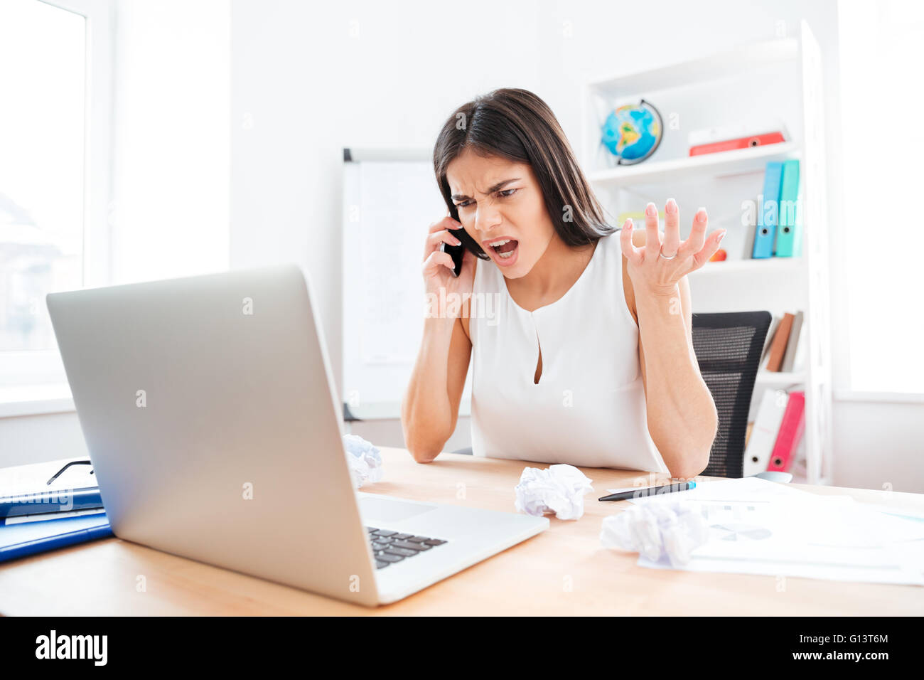 Arrabbiato imprenditrice parlando al telefono in ufficio Foto Stock