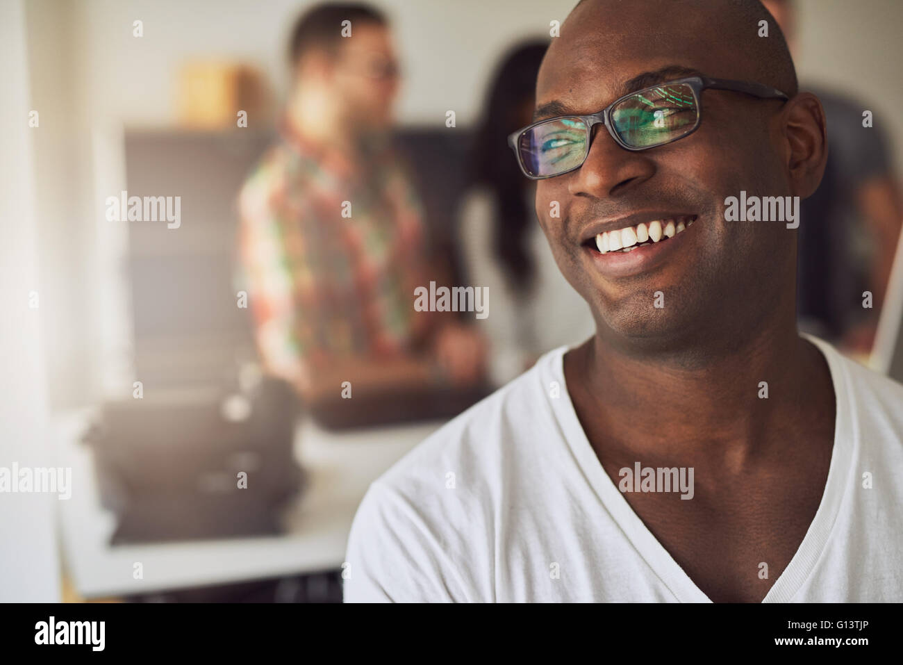 Close up bello sorridente lavoratore in una camicia bianca e occhiali con tre fuori fuoco dipendenti dietro di lui in riunione Foto Stock