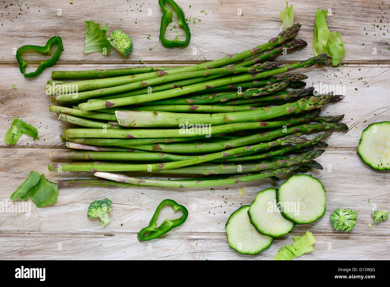 Alta angolazione di alcune diverse materie vegetali verdi come il pepe verde, asparagi, broccoli o le zucchine, su un bianco rustico Foto Stock