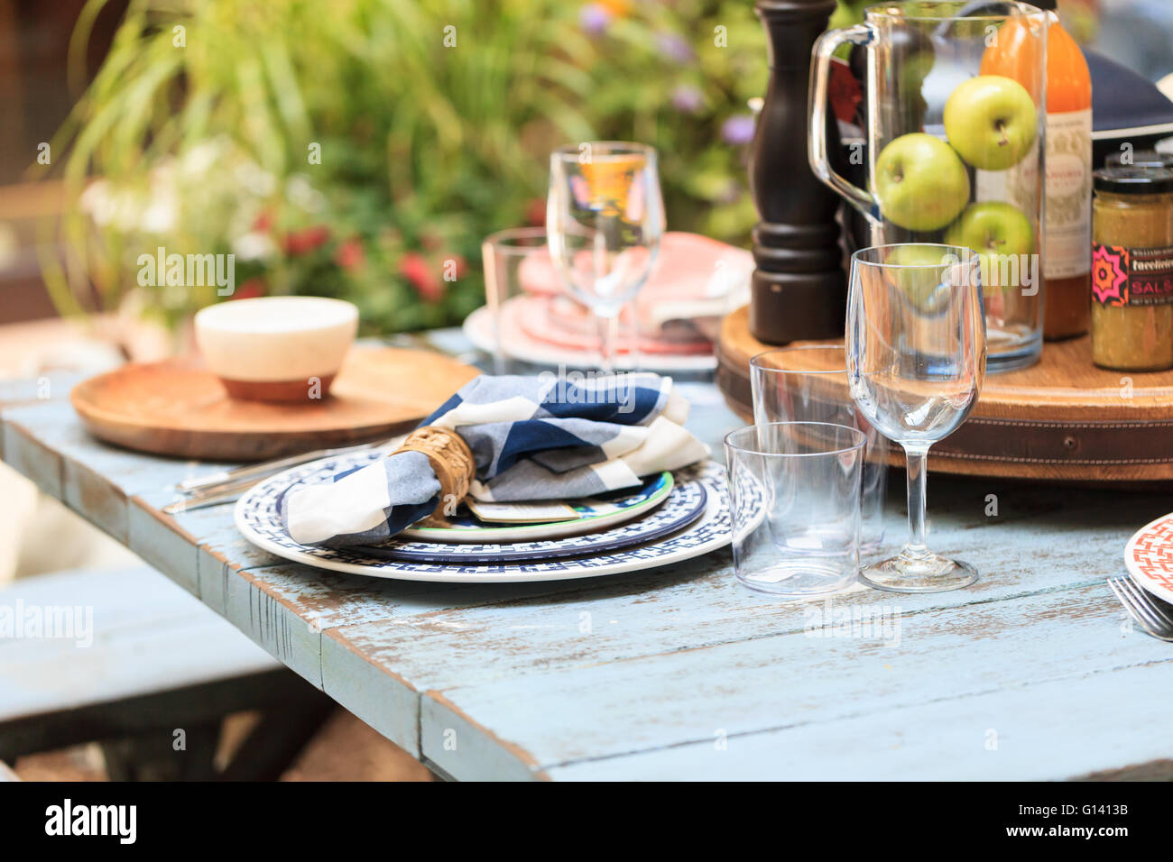 Agriturismo Rustico posto impostazione di bianco e blu con piastre, tovaglioli e chiaro bicchieri di vino in un paese invecchiato tavolo su un patio in Foto Stock