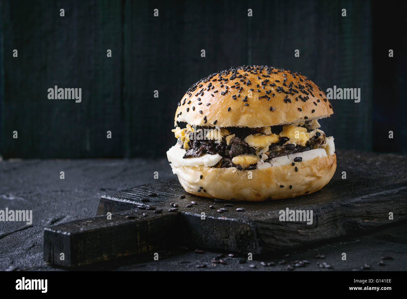 In casa hamburger vegetariano con riso nero, il formaggio halloumi e uova strapazzate, servita sul tagliere di legno su nero testurizzato b Foto Stock