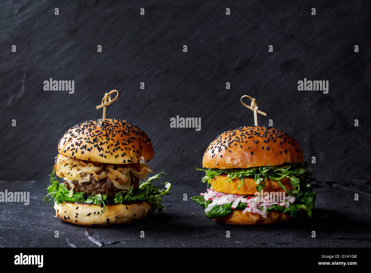 In casa tradizionale e veggie hamburger con carne di manzo, cipolla fritti, patata dolce, ravanello e germogli di piselli, servita su nero testurizzato Foto Stock