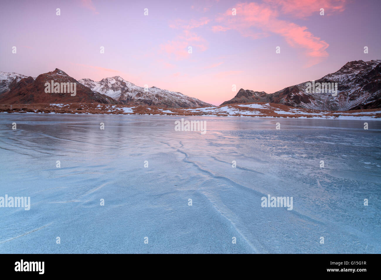 Luci rosa di alba sulle cime innevate intorno alla superficie ghiacciata del lago Andossi, Valle Spluga, Valtellina, Lombardia, Italia Foto Stock