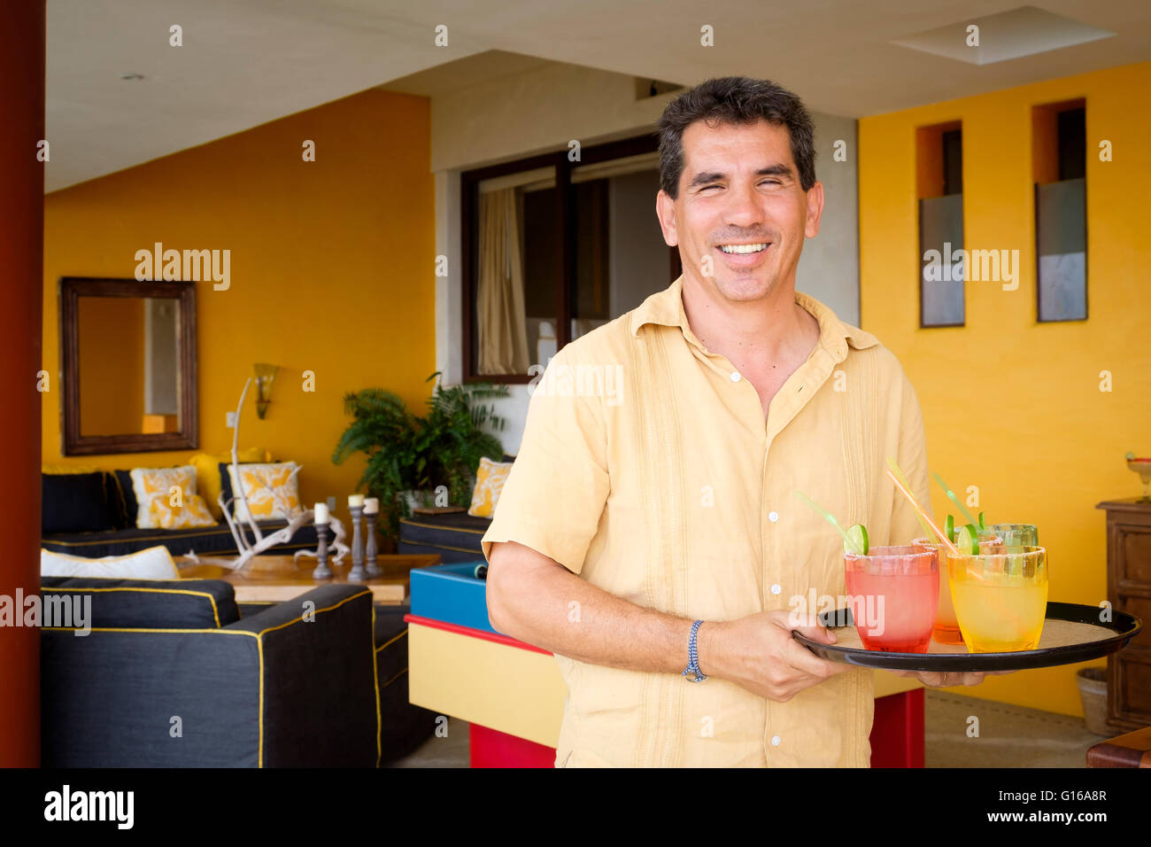 Sorridente uomo ispanico, 50 anni, serve cocktail su un vassoio Foto Stock