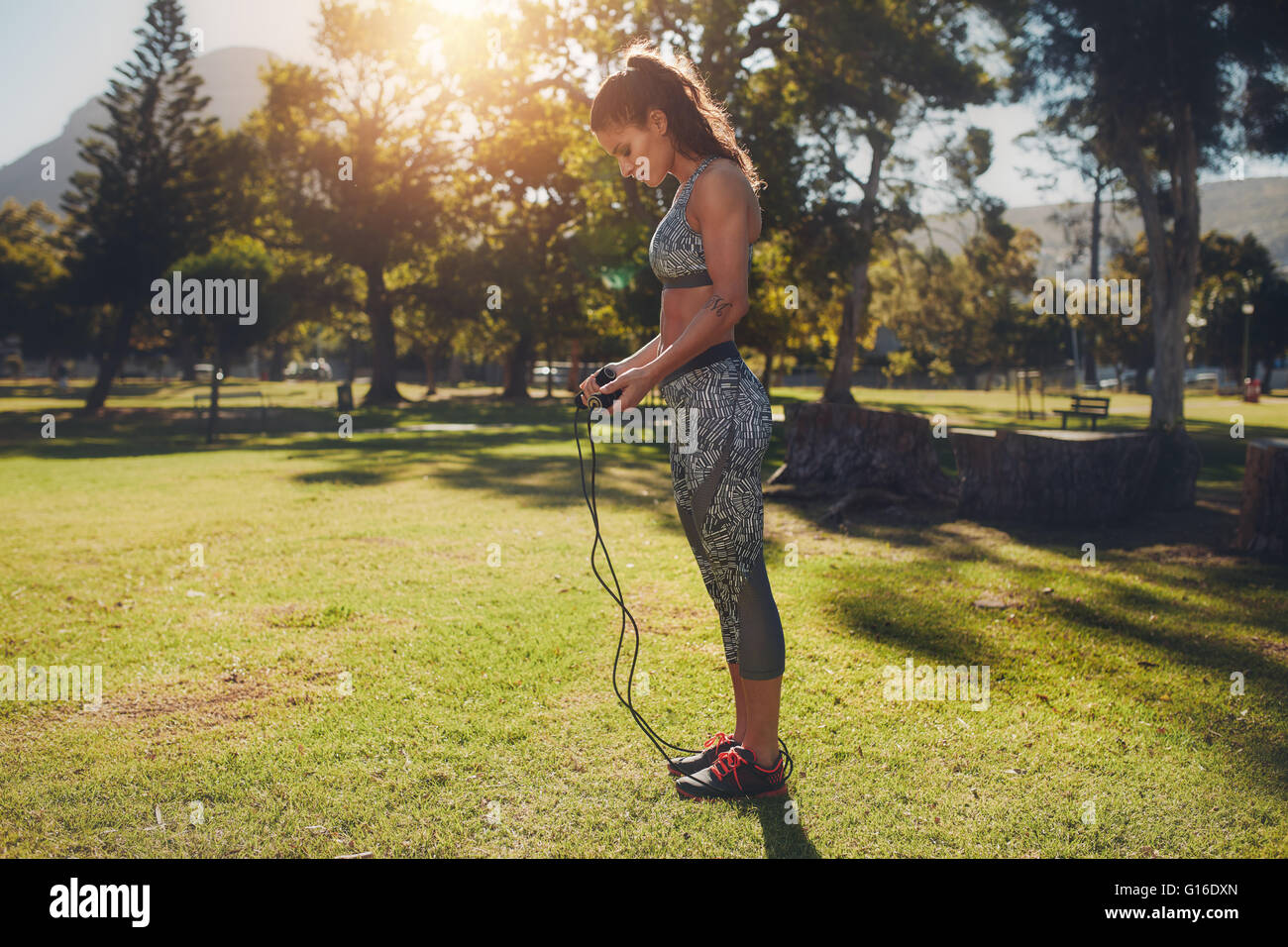 Foto a tutta lunghezza di una giovane donna in forma con corda per saltare all'aperto nel parco. donna fitness che tiene una corda per saltare per l'allenamento su s. Foto Stock