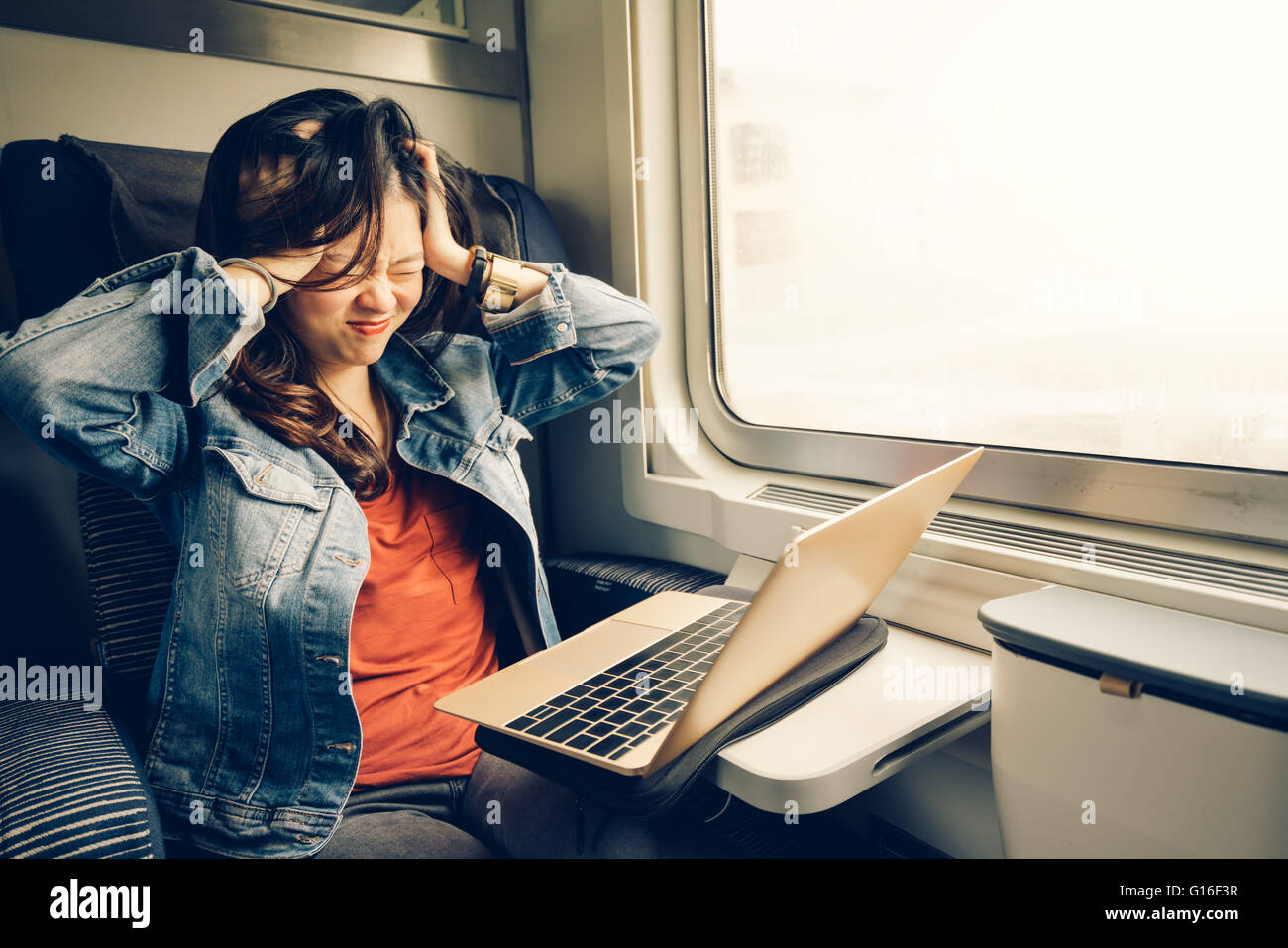 Asian college girl frustrati con il computer portatile sul treno, luce calda tonalità, con spazio di copia Foto Stock