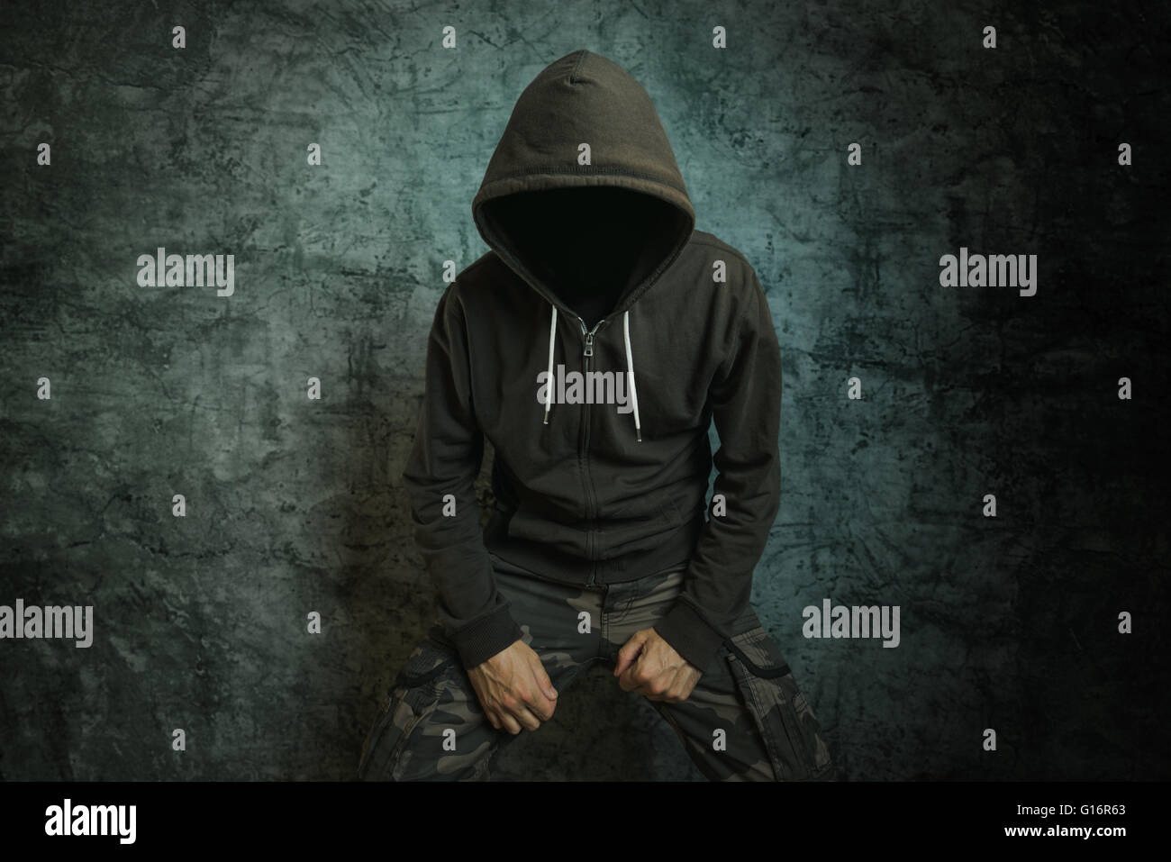 Spooky male persona criminale con giacca con cappuccio nella parte anteriore della parete di cemento. Foto Stock