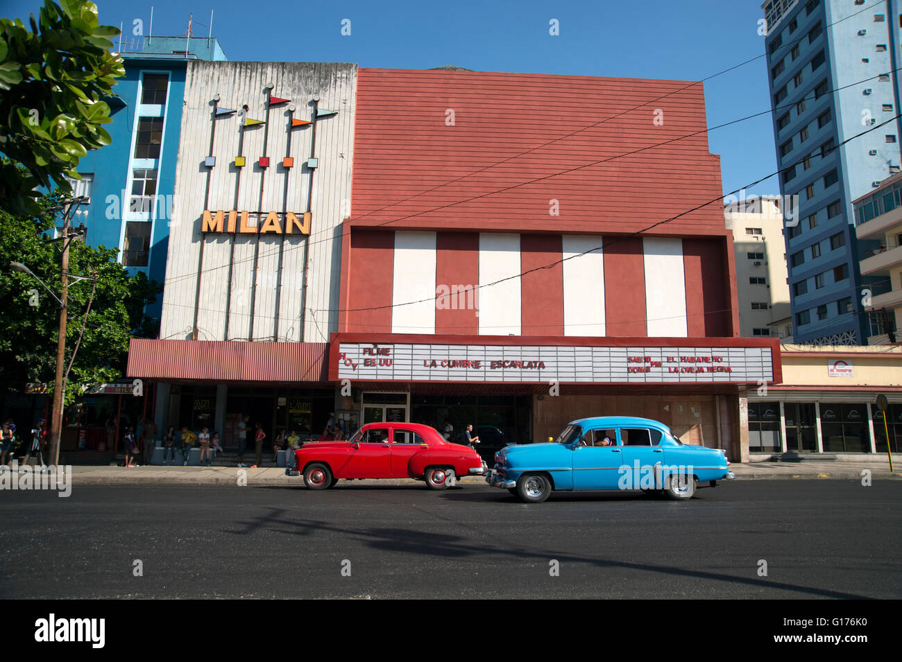Due vecchi anni cinquanta vetture americane più di sinistra dopo la rivoluzione guidare passato un cinema Art-Deco edificio nel Vedado Avana Cuba Foto Stock