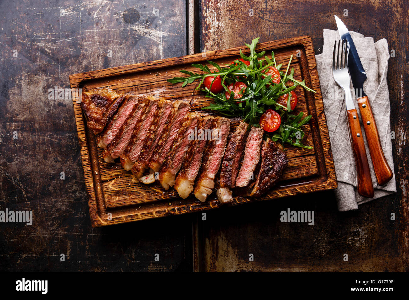 Fette di manzo alla griglia barbecue bistecca di controfiletto con insalata e pomodori e rucola sul bordo di taglio su sfondo scuro Foto Stock