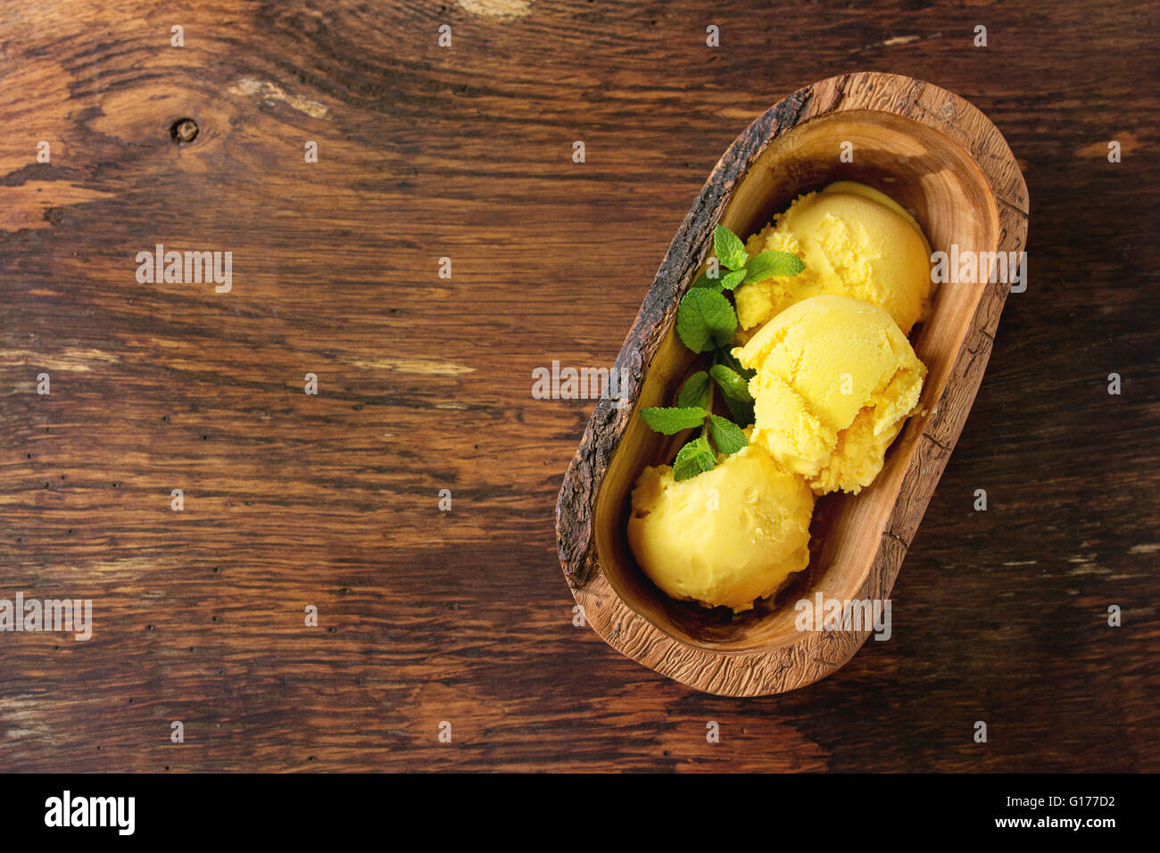 In casa Gelato al mango con menta fresca in legno d'olivo ciotola, servita in legno sfondo a trama. Vista da sopra con lo spazio di copia Foto Stock