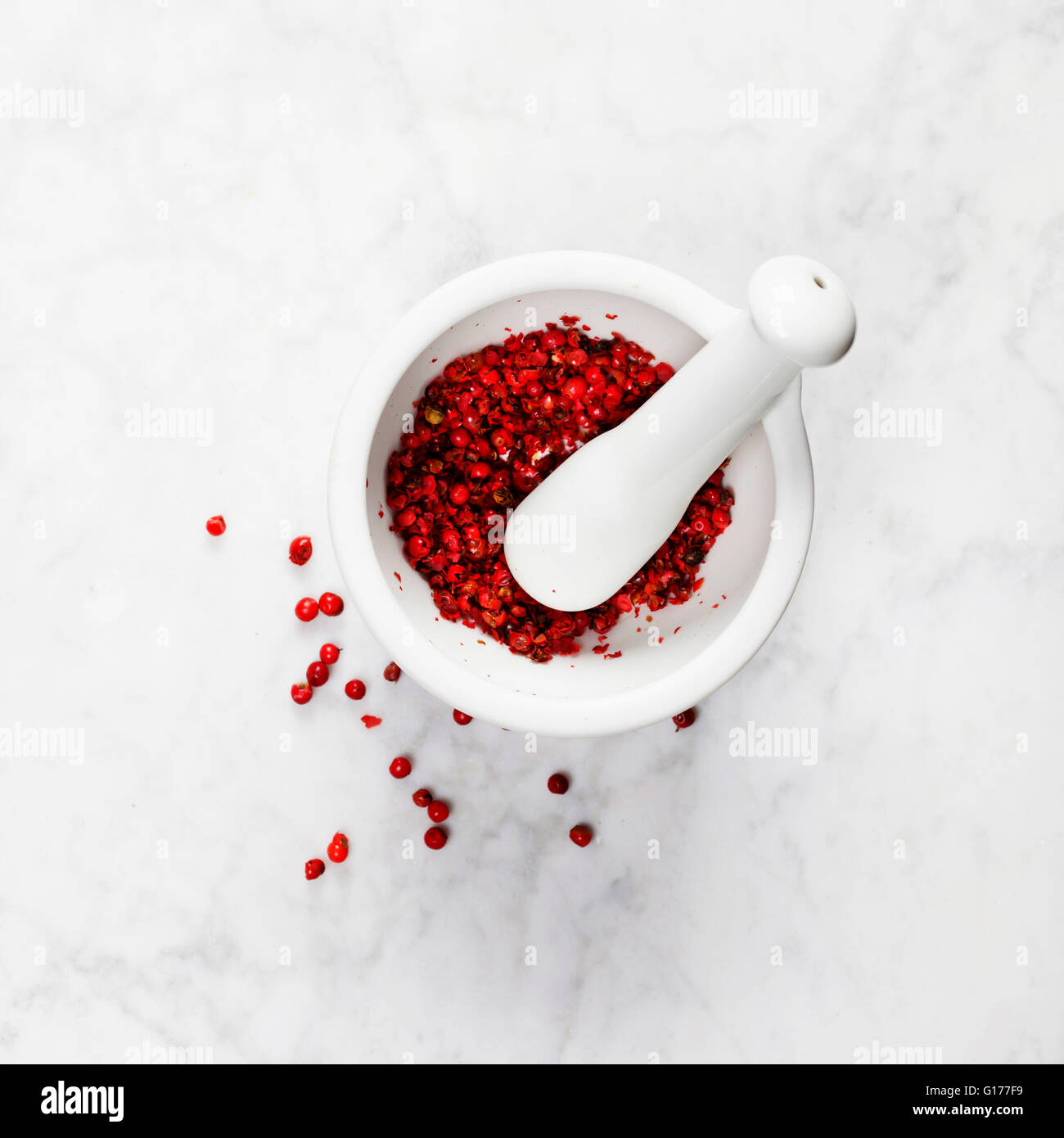 Mortaio e pestello con grani di pepe rosso su sfondo marmo Foto Stock