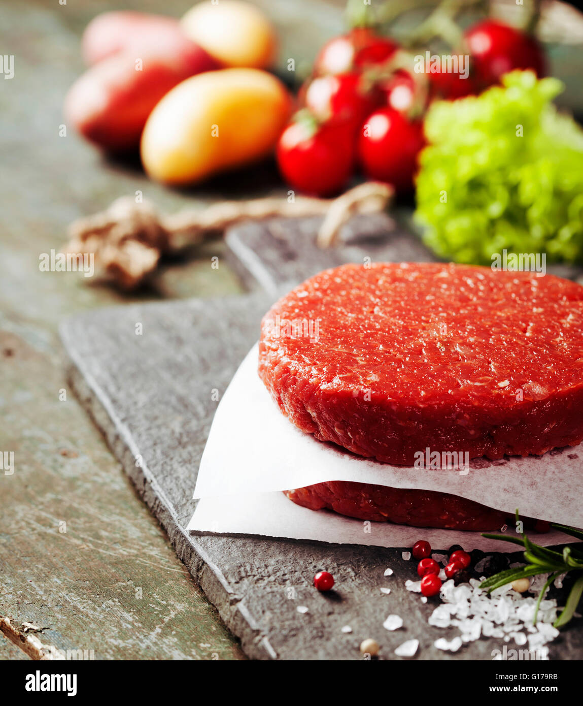 Materie di macinato di manzo hamburger di carne costolette di manzo con il condimento e verdure su vintage di tavole di legno Foto Stock