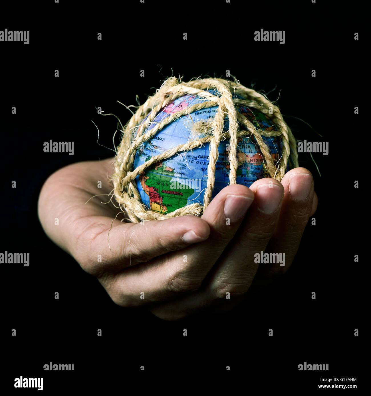 Primo piano di un giovane uomo con un globo mondo nella sua mano legata con corda, con un effetto drammatico Foto Stock