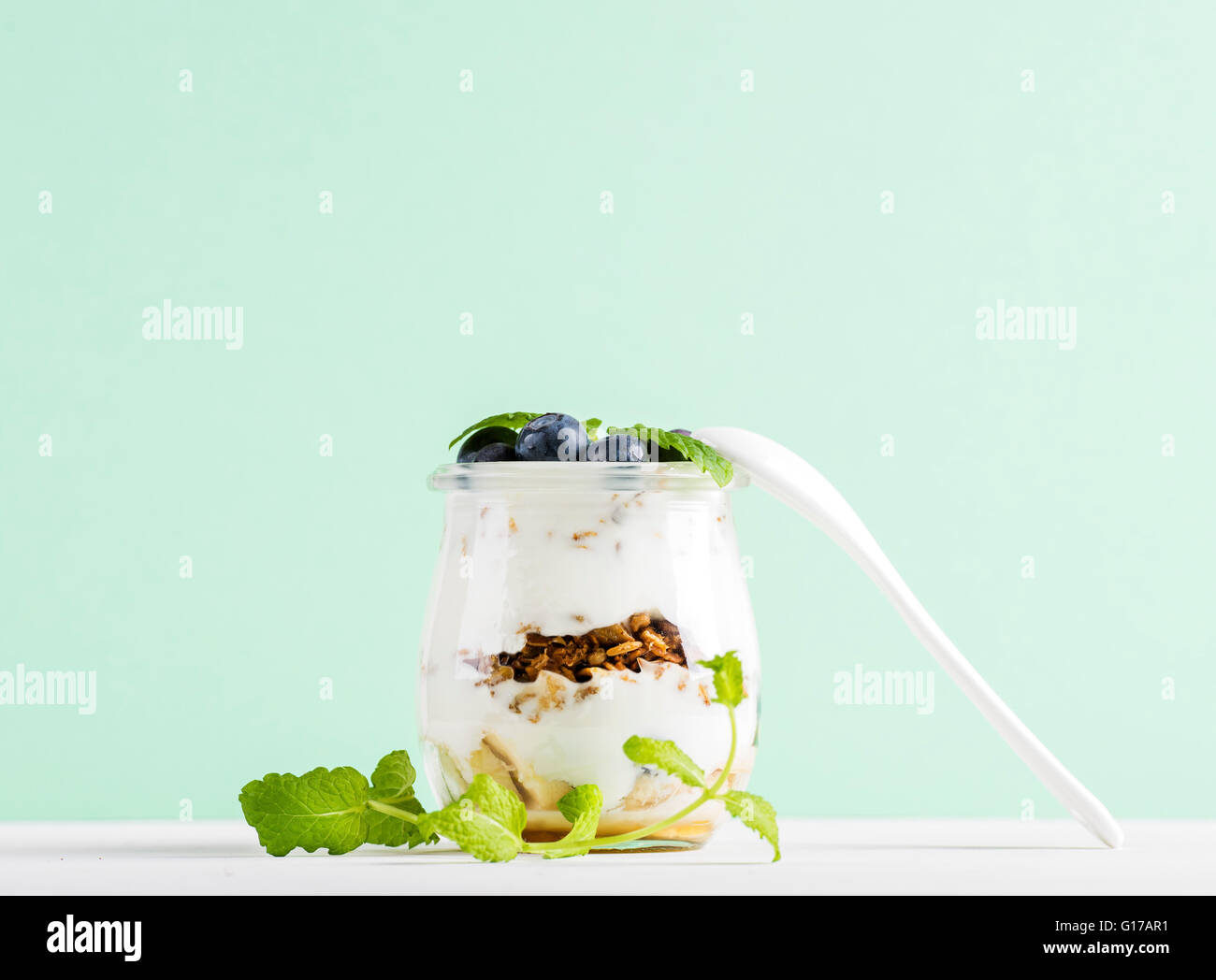 Yogurt oat granola con frutti di bosco freschi e le foglie di menta in un barattolo di vetro sul cemento grigio Sfondo testurizzata Foto Stock