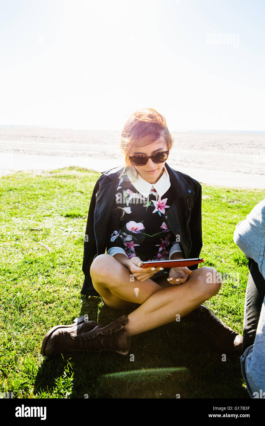 Giovane donna seduta zampe trasversale sull'erba, guardando a tavoletta digitale Foto Stock