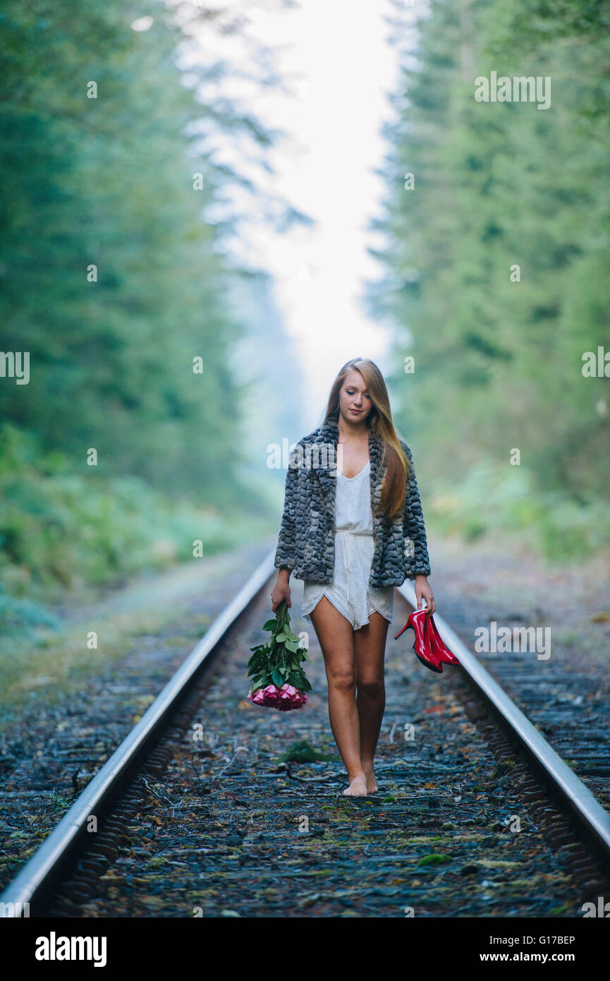 Ragazza adolescente, passeggiate lungo via treno, tenendo red shoes e fiori Foto Stock