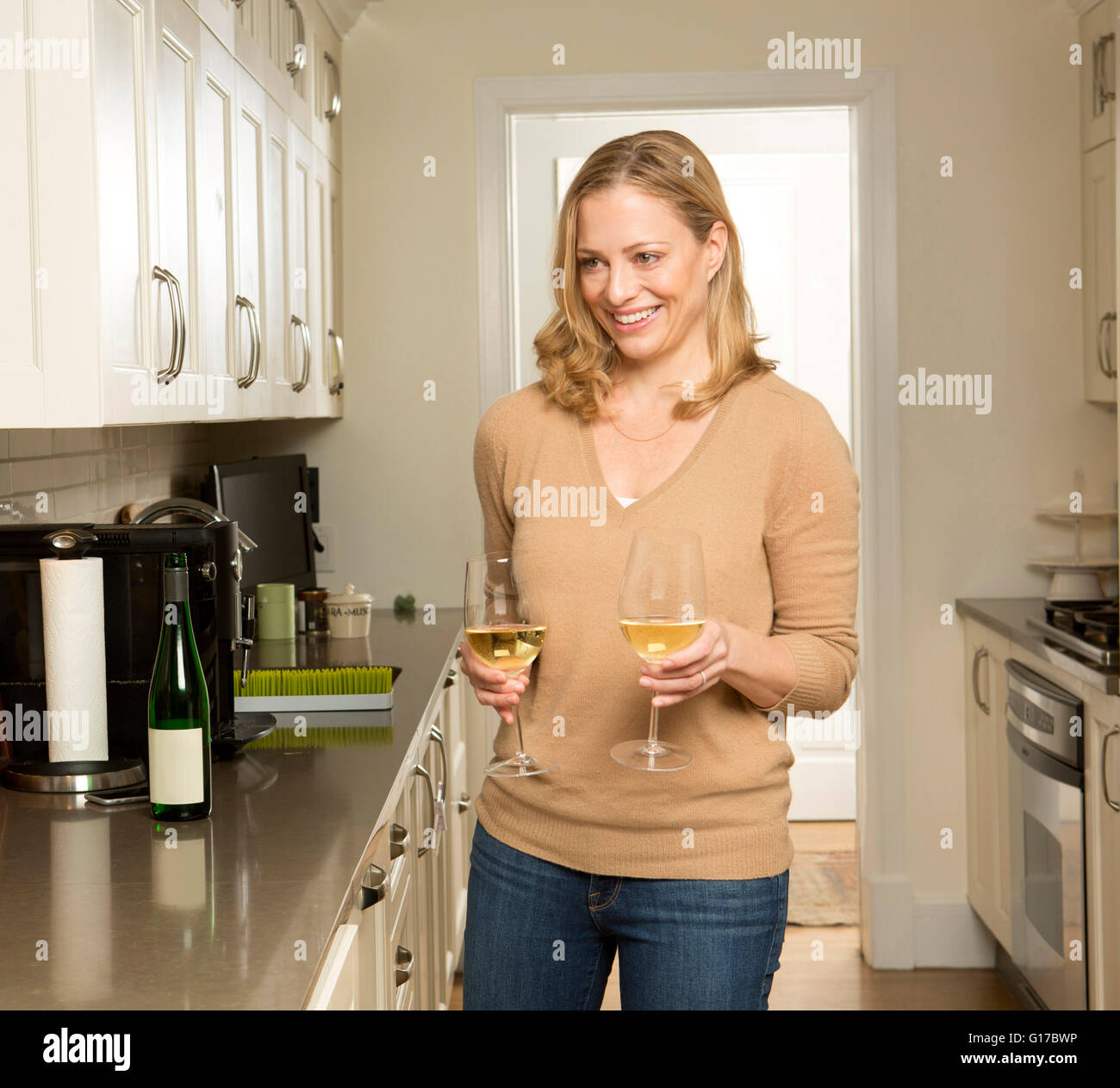 La donna che porta due bicchieri di vino bianco in cucina Foto Stock