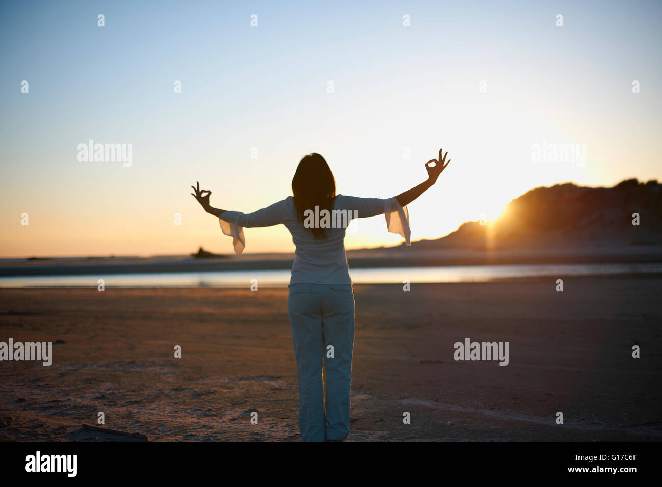 Vista posteriore della donna con le braccia aperte sul Cannon Beach al tramonto, CALIFORNIA, STATI UNITI D'AMERICA Foto Stock