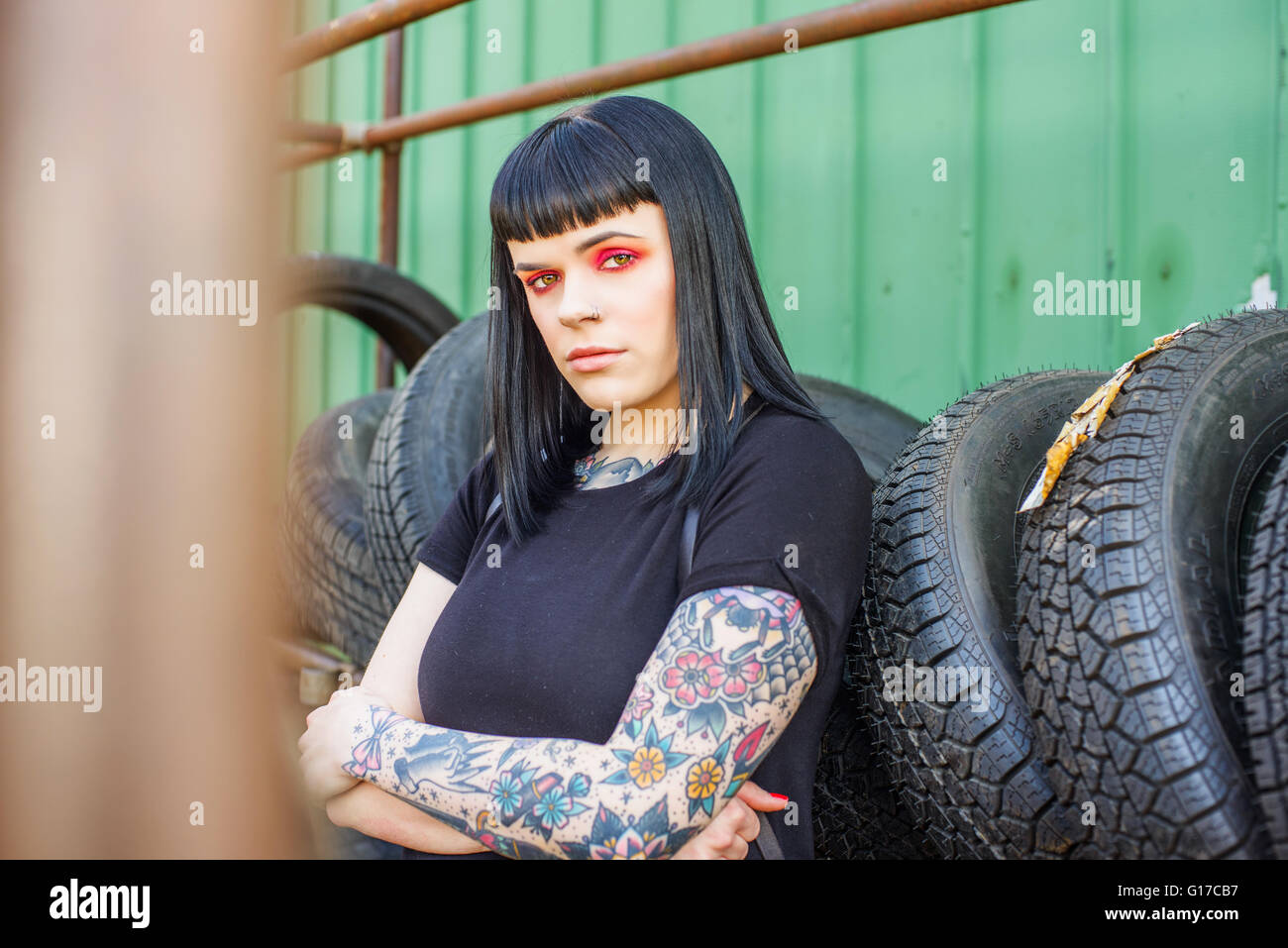 La donna tatuata appoggiata contro i pneumatici con le braccia incrociate guardando la fotocamera Foto Stock