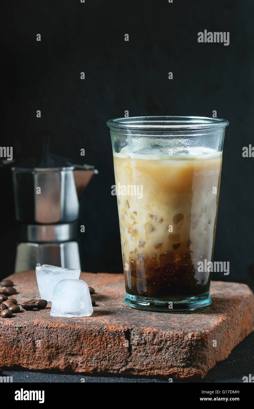 Bicchiere di ghiaccio caffè con panna e latte servita con i chicchi di caffè, i cubetti di ghiaccio e la caffettiera sulla scheda di pietra sopra nero testurizzato b Foto Stock