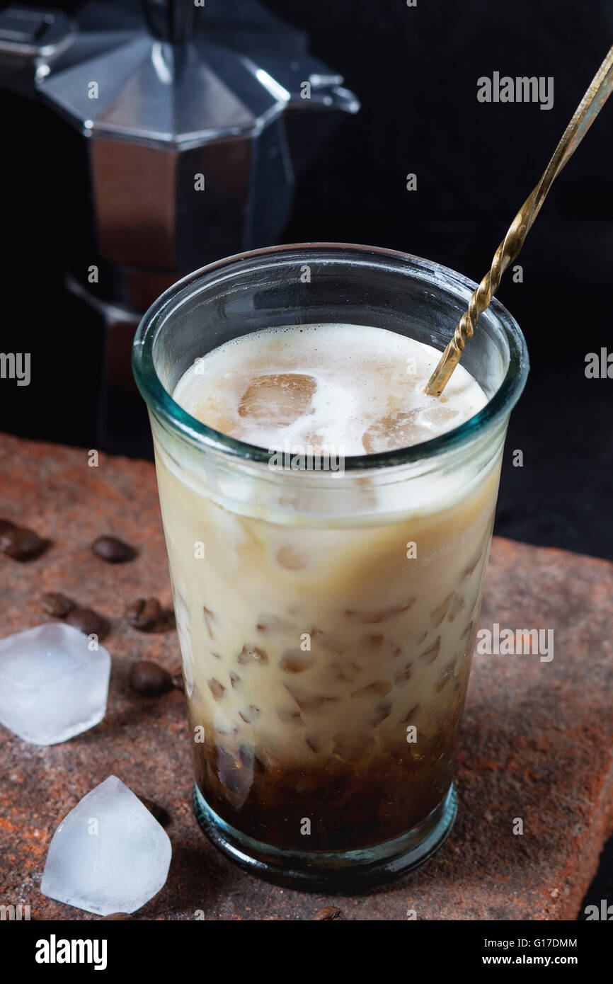 Bicchiere di ghiaccio caffè con panna e latte servita con i chicchi di caffè, i cubetti di ghiaccio e la caffettiera sulla scheda di pietra sopra nero testurizzato b Foto Stock