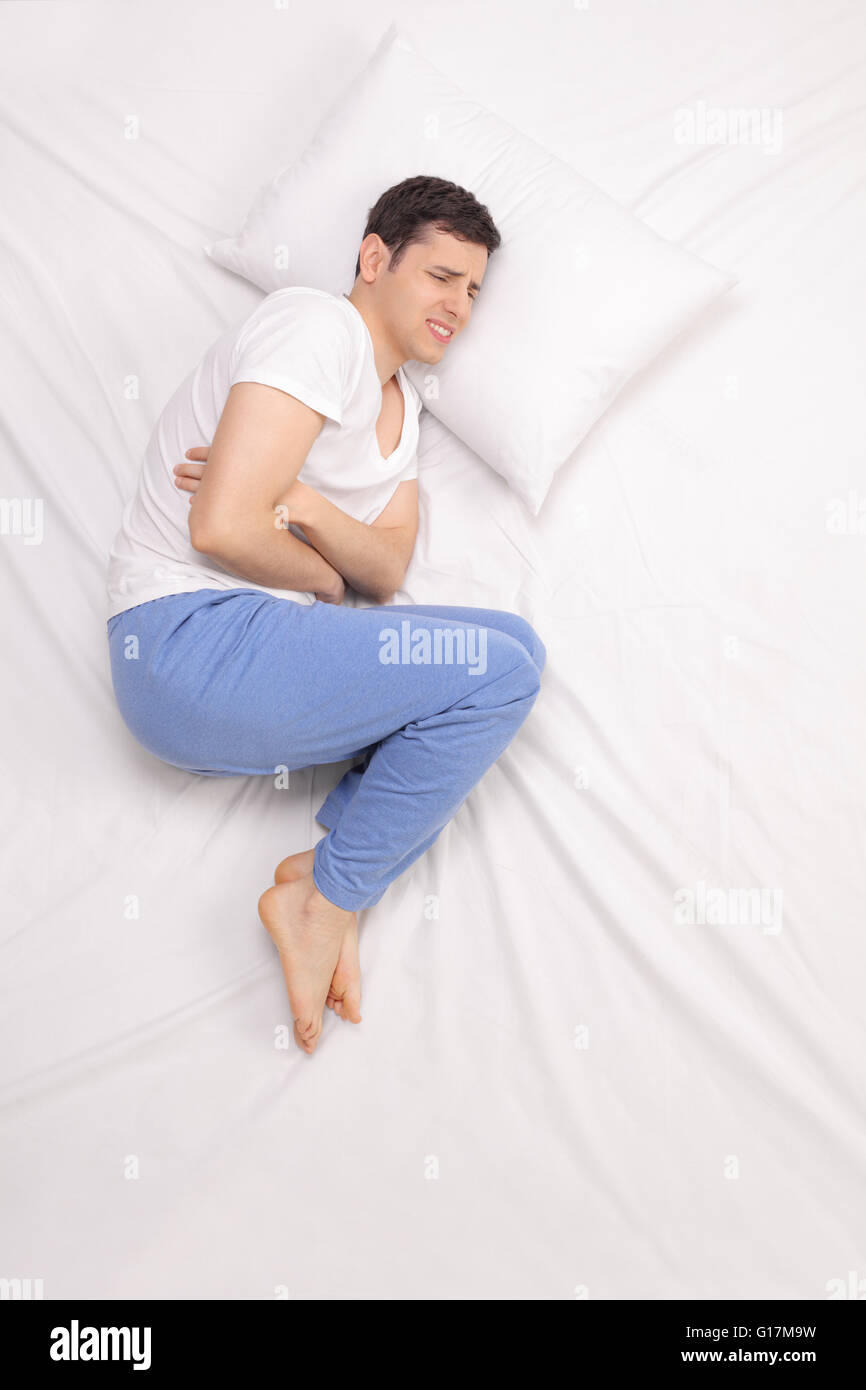 Colpo verticale di un giovane uomo che stabilisce nel letto e sperimentare mal di stomaco Foto Stock