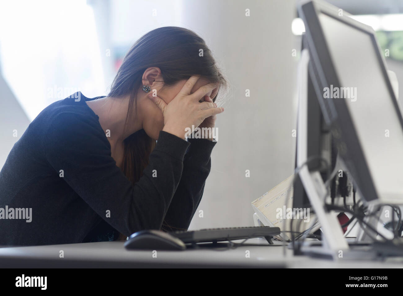 Vista laterale della donna seduta al computer in testa le mani Foto Stock